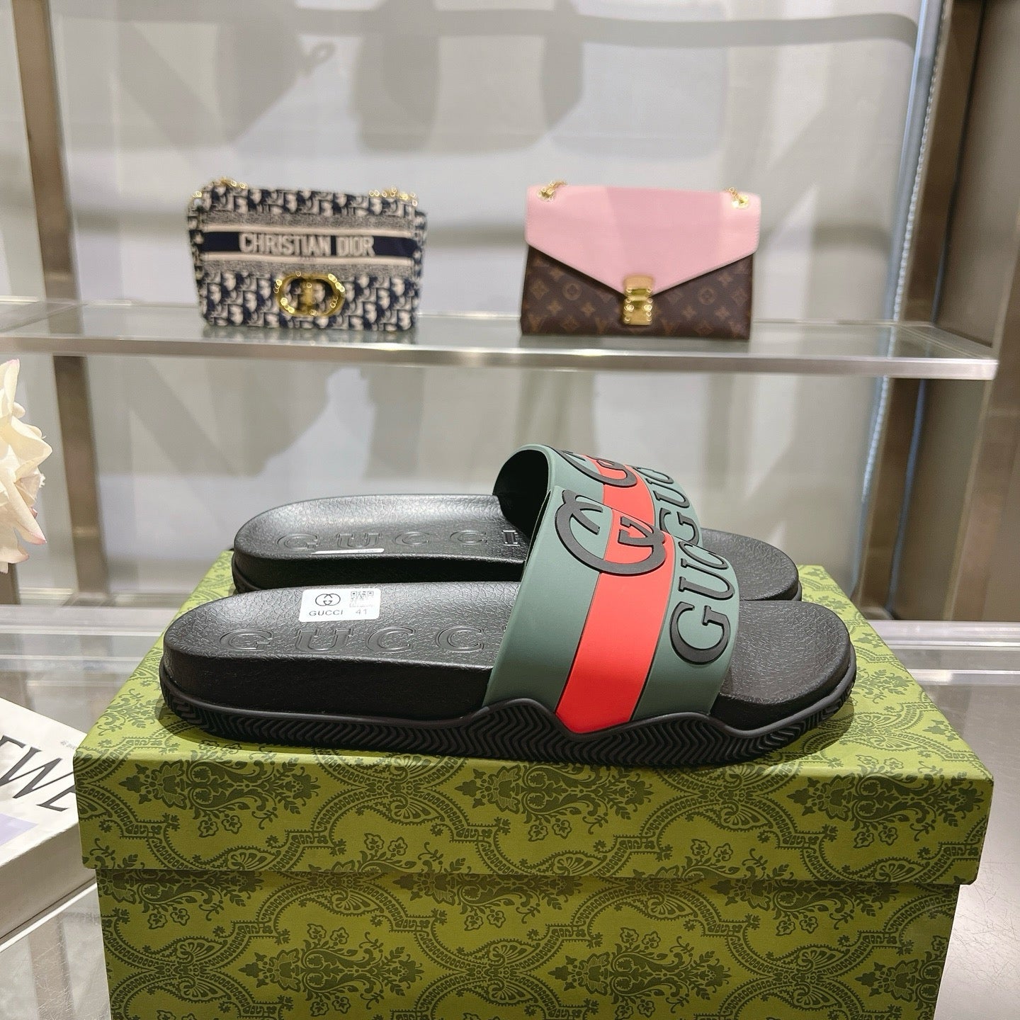 Black Gucci slide sandals with green strap and red stripe on textured footbed.