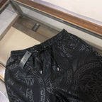 Versace black drawstring shorts with elastic waistband and repeating geometric pattern.