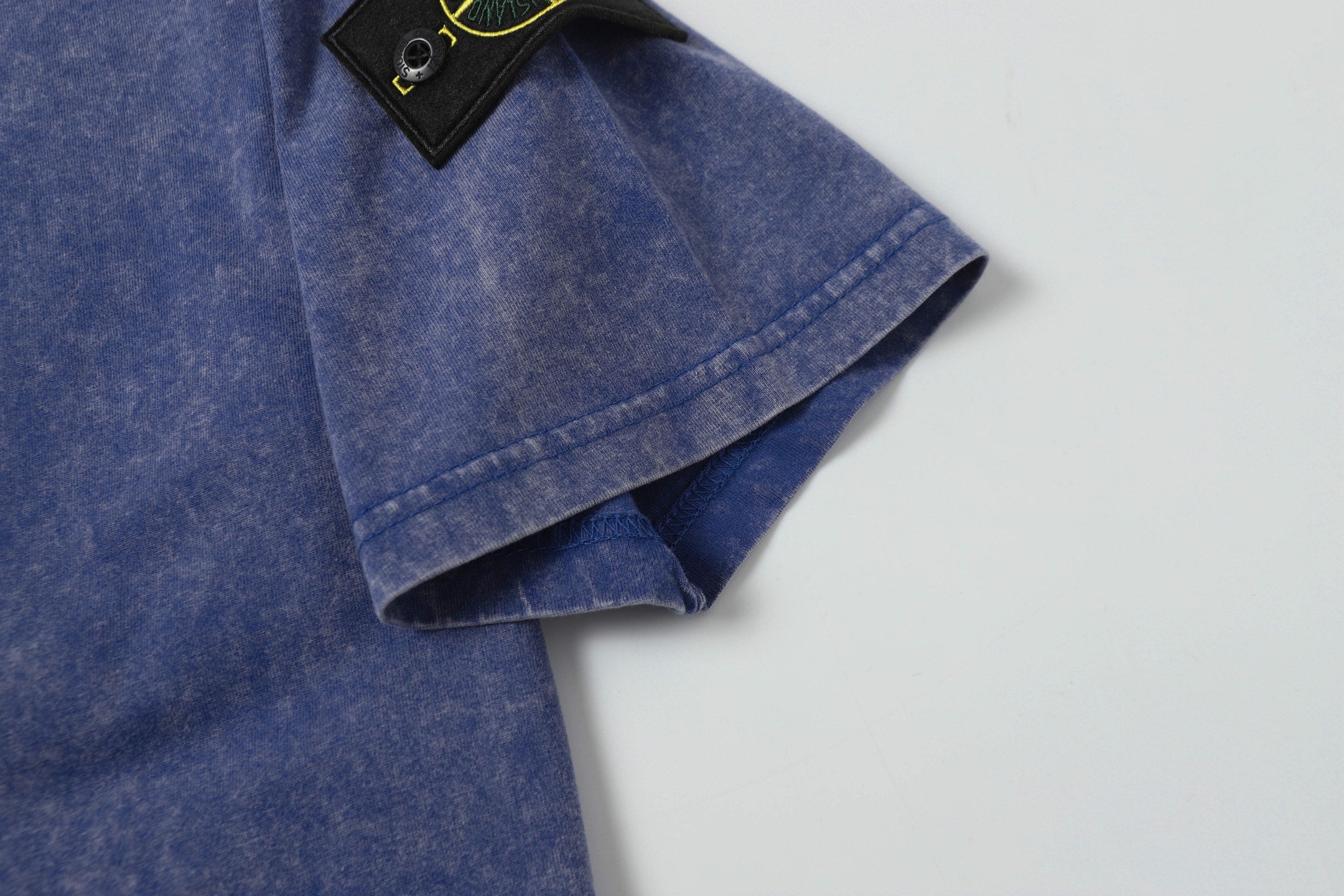 Blue T-shirt hem with logo patch corner and folded sleeve cuff.