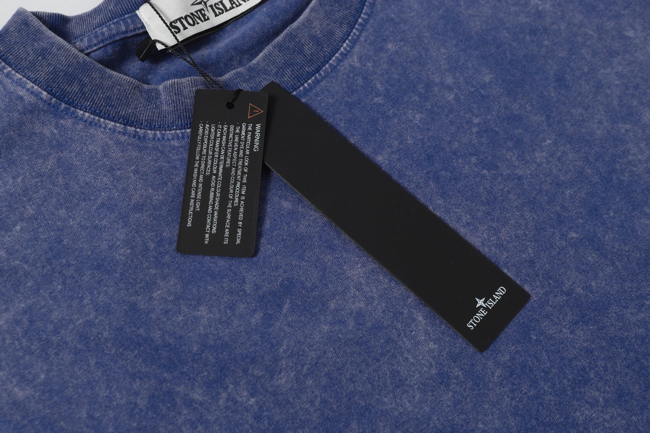 Blue crew-neck T-shirt collar with Stone Island neck label and hang tag.