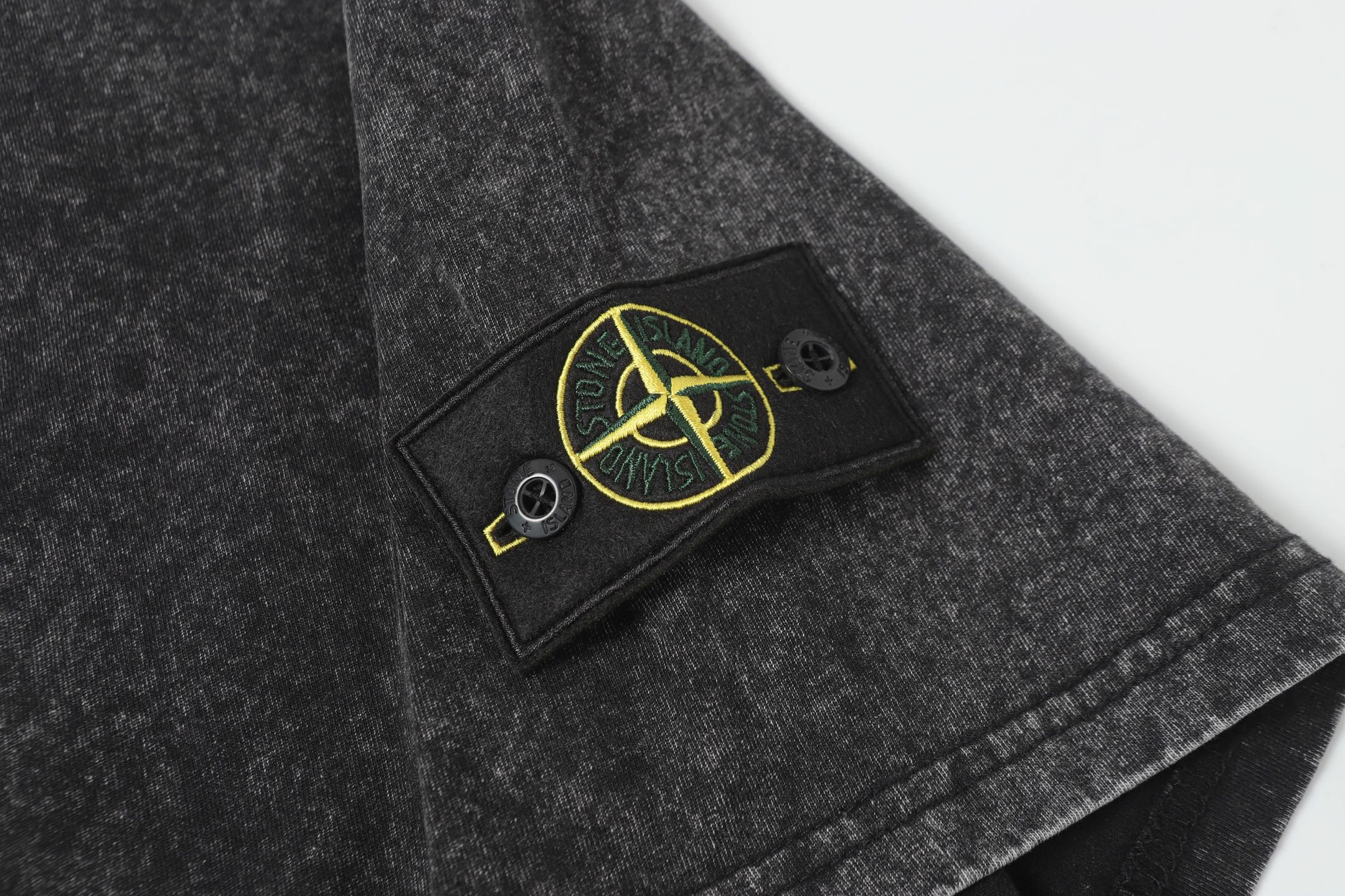 Dark charcoal T-shirt chest patch with yellow emblem and two visible buttons