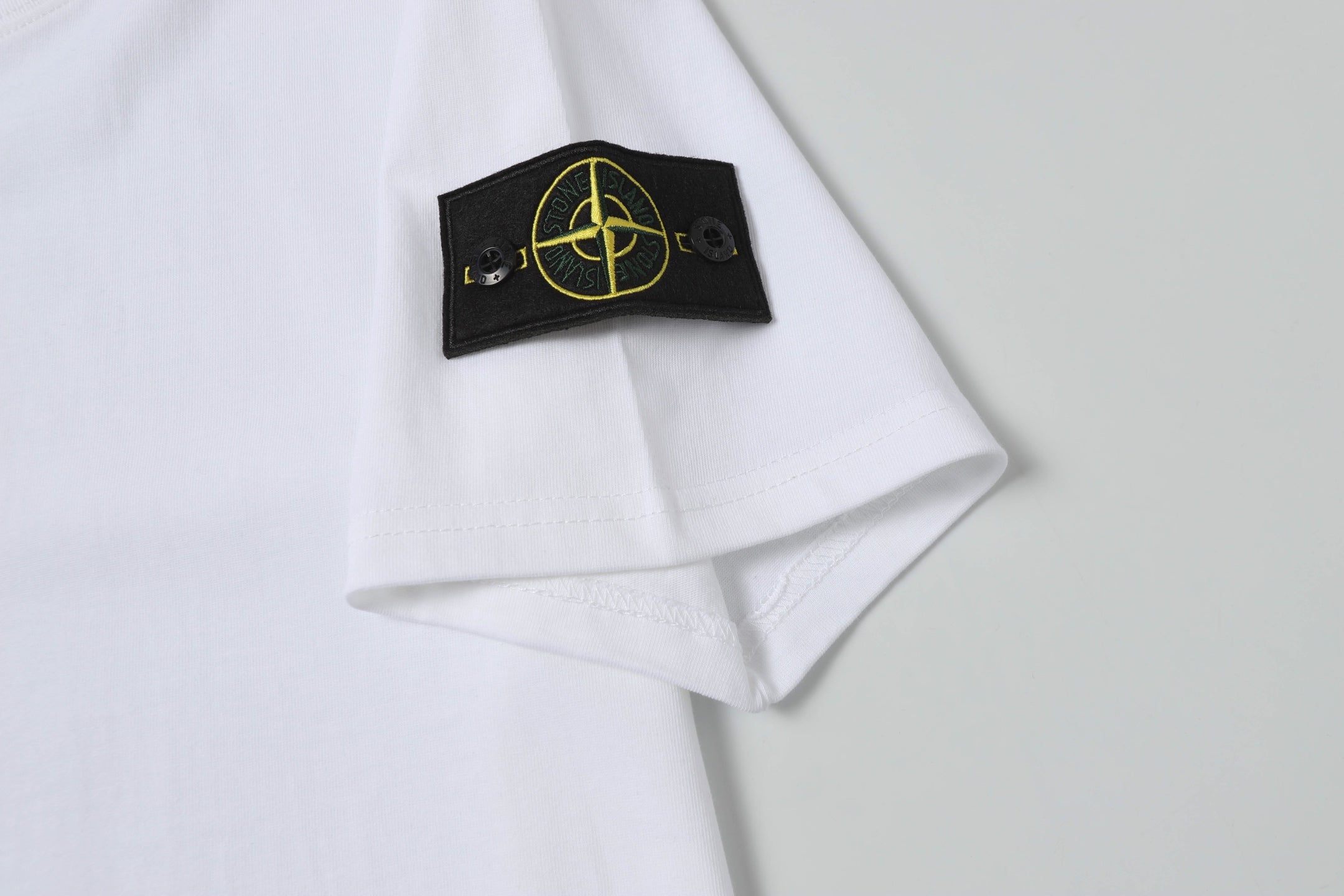 White Stone Island T-shirt sleeve cuff with black gold logo patch.