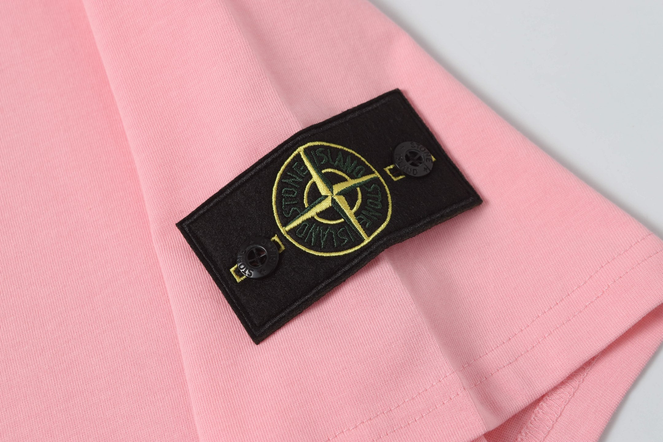 Pink T-shirt with black sleeve patch featuring yellow Stone Island emblem