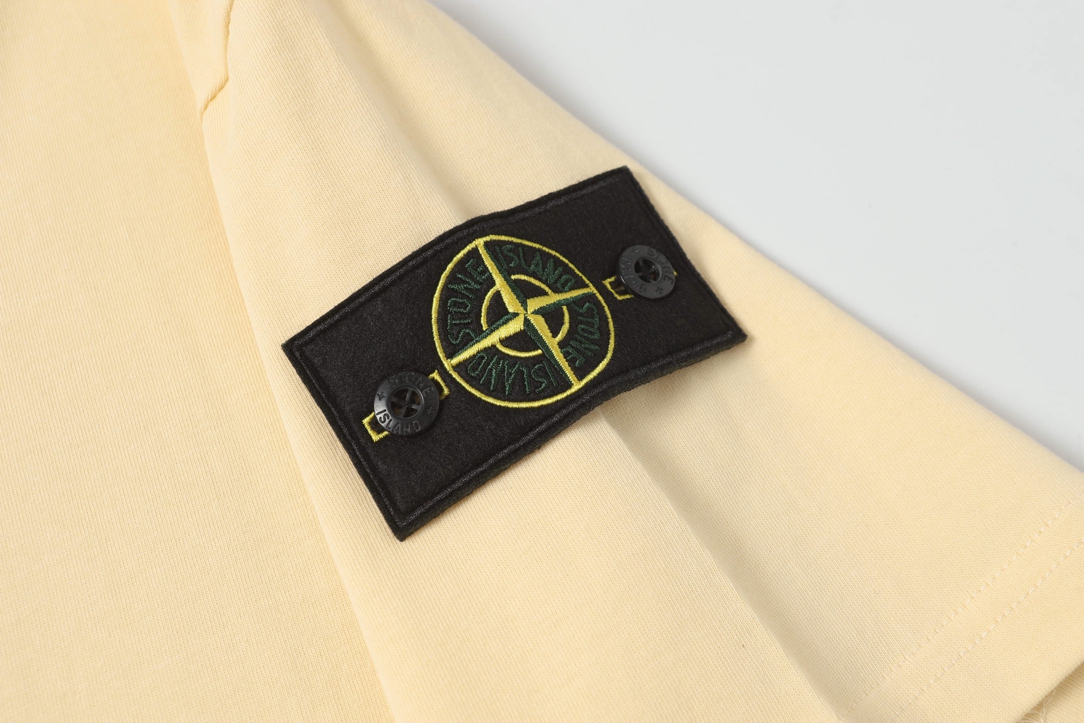 Cream T-shirt with black logo patch detail near the sleeve