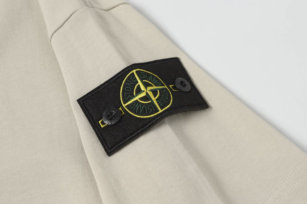 Light beige T-shirt sleeve with black patch detail and yellow logo