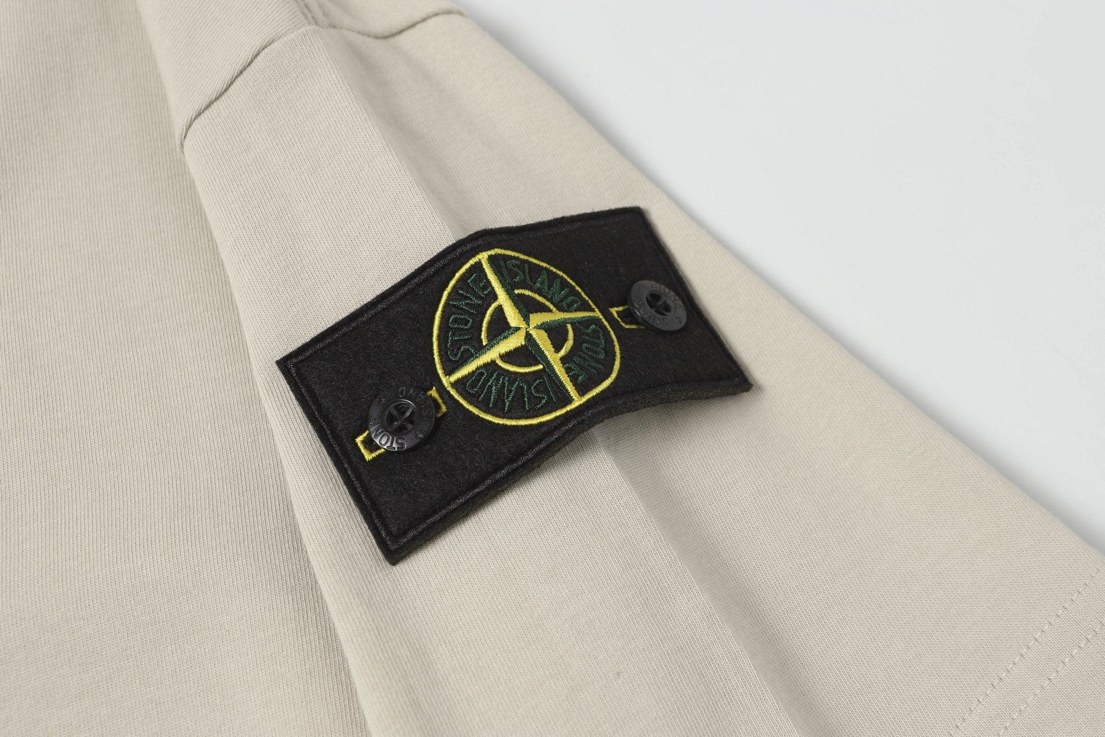Light beige T-shirt sleeve with black patch detail and yellow logo