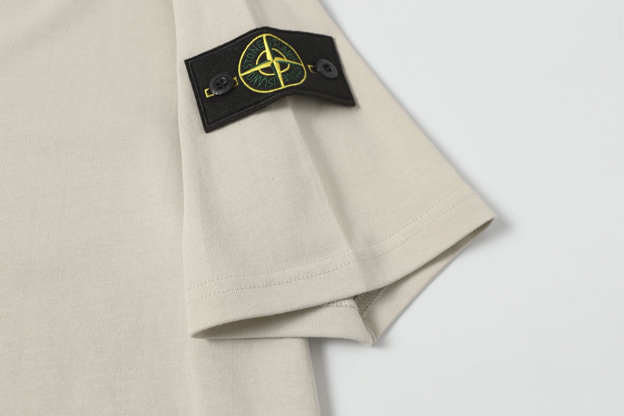 Light beige T-shirt sleeve with black patch and yellow logo