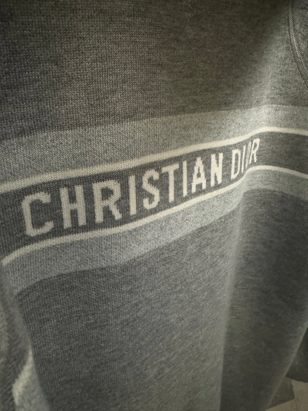 Close-up of CHRISTIAN DIOR logo stripe on gray hoodie