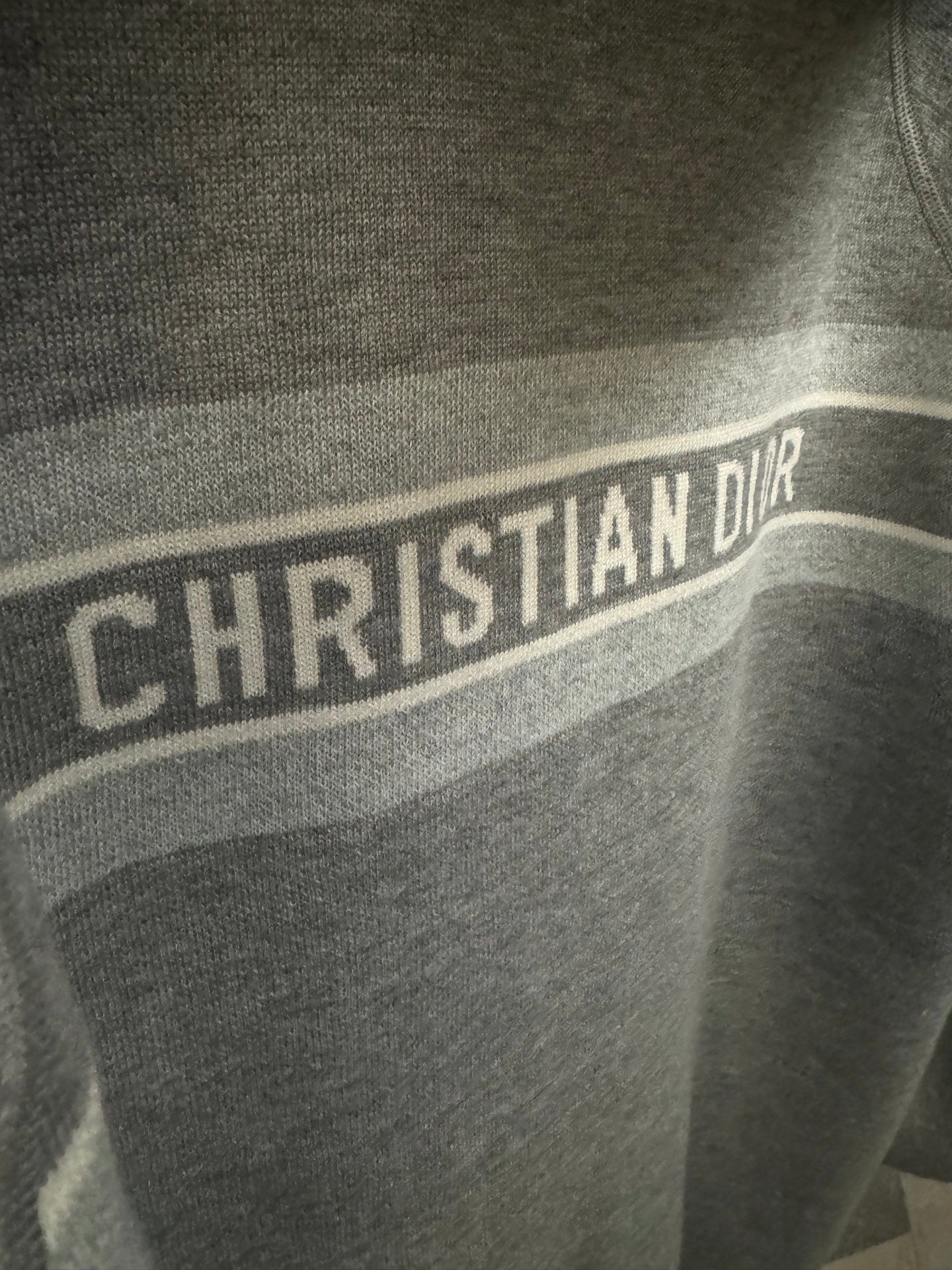 Close-up of CHRISTIAN DIOR logo stripe on gray hoodie
