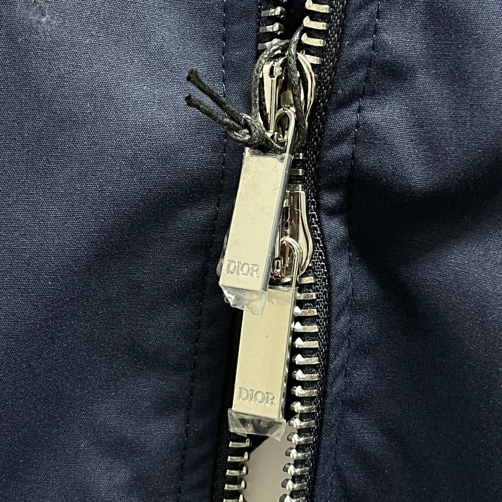 Navy bomber jacket close-up of silver zipper and metal zip pull with tags.