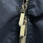 Navy bomber jacket close-up of silver zipper and metal zip pull with tags.