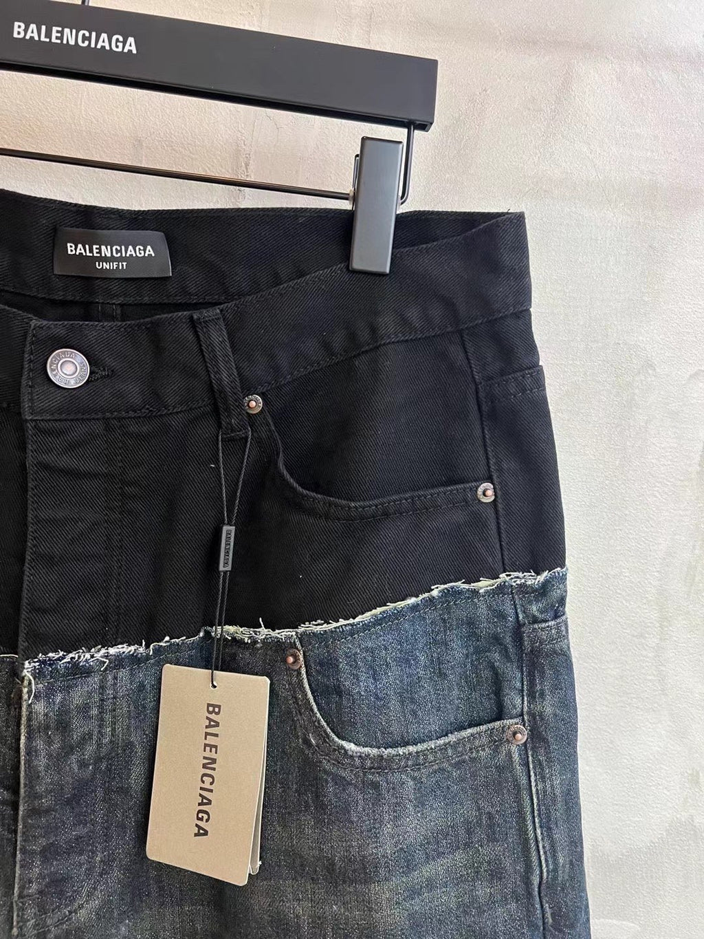 Black denim jeans with front pockets, metal buttons, and frayed hem detail with patch.
