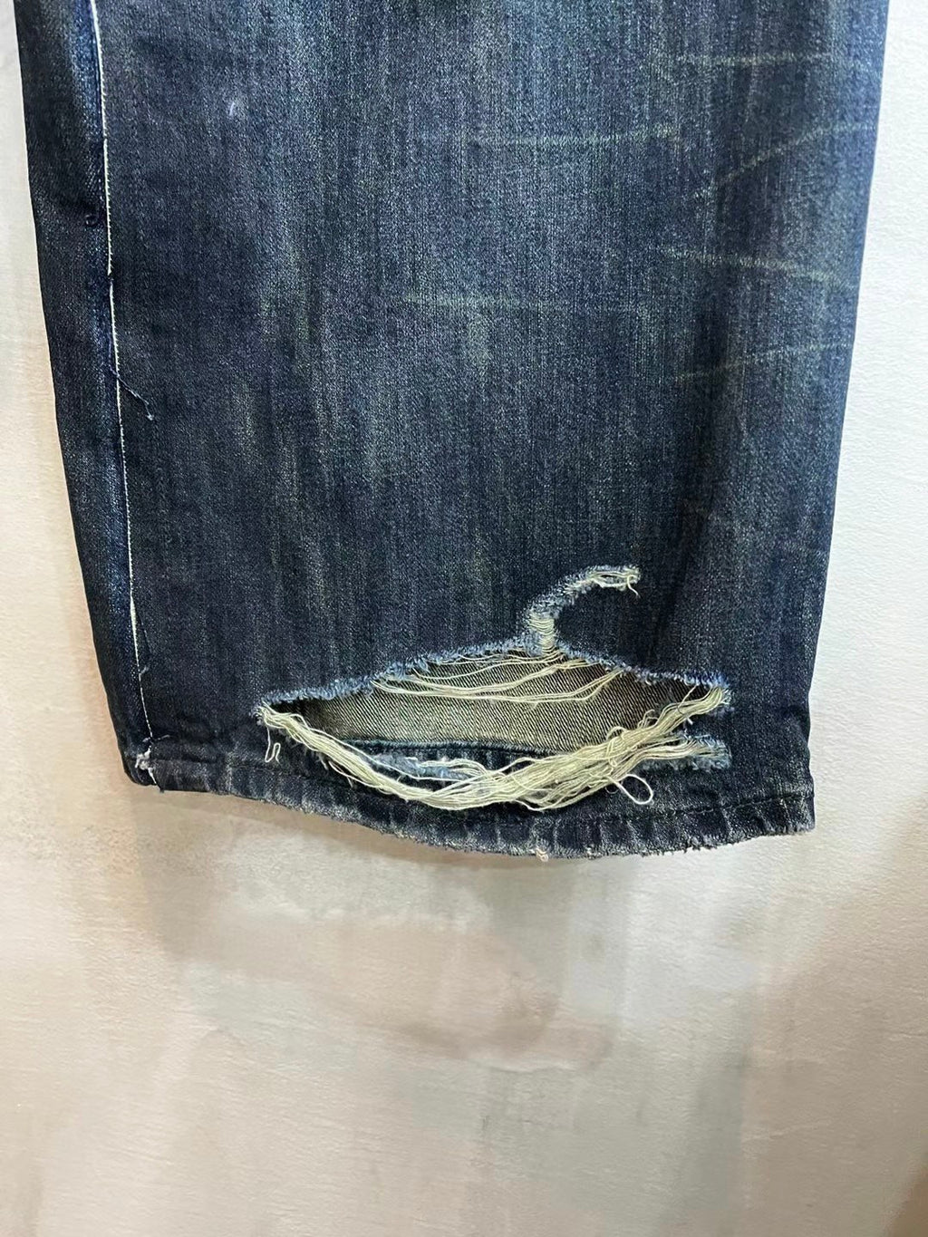 Denim jeans bottom hem with frayed edge and overlocked repairs at the cuff.