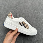 White low-top sneakers with plaid side detail, visible stitching, and blue sole accent