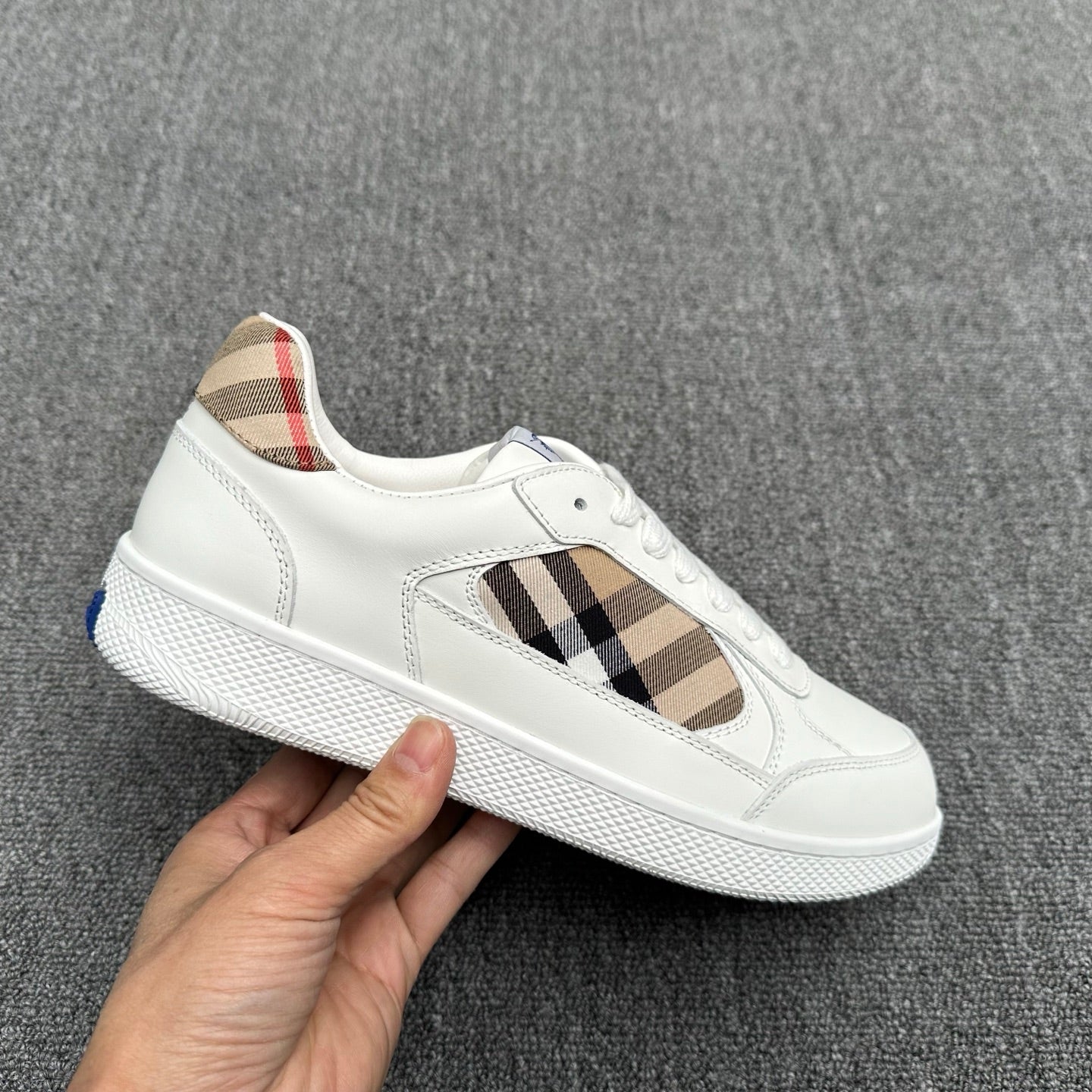 White low-top sneakers with plaid side detail, visible stitching, and blue sole accent