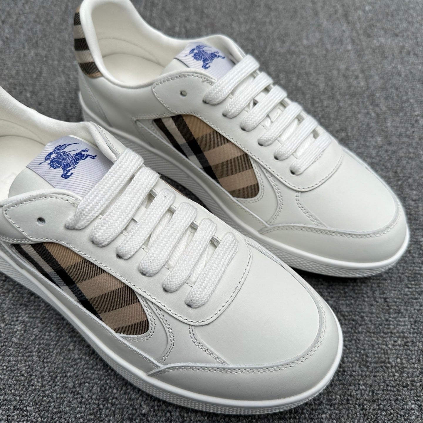 Close-up of white lace-up sneakers with plaid side panel and blue horse logo