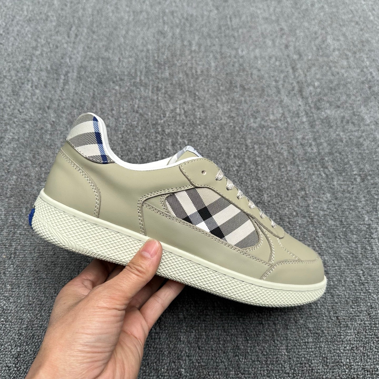 Burberry low-top sneaker held by hand, beige leather with check inlay and blue lining