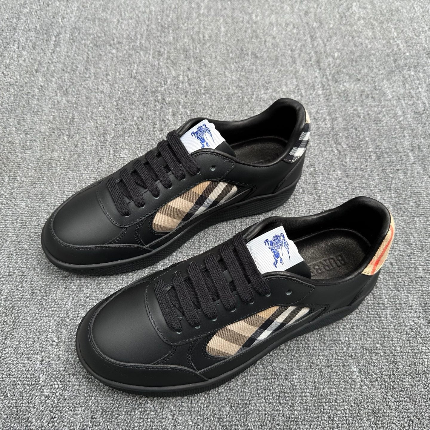 Black low-top sneakers with beige plaid side stripe and blue logo patch