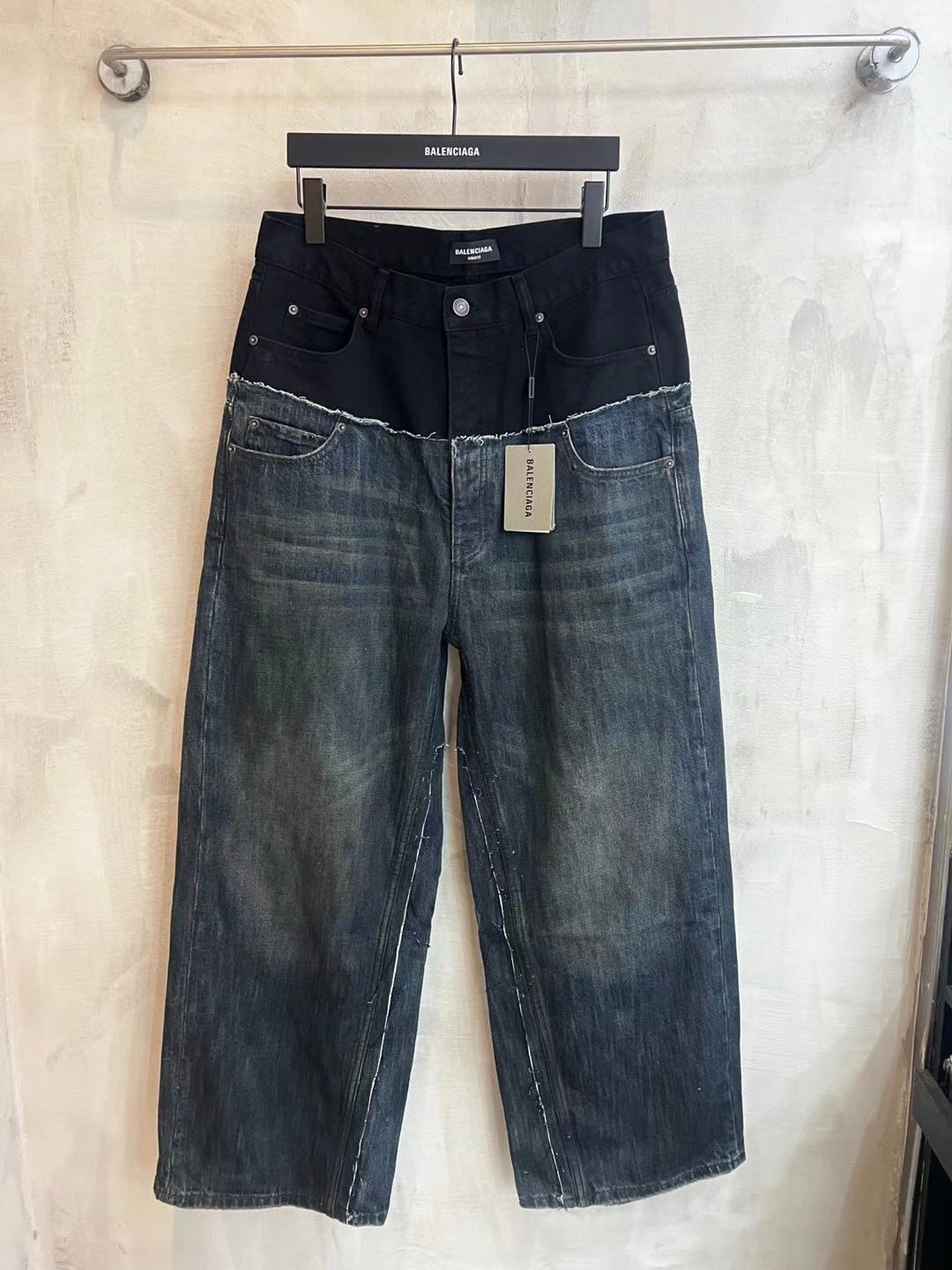 Two-tone denim jeans with dark upper, patchwork panels, and distressed hem at bottom.
