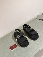 Black Gucci sandals on display with gold-tone GG buckles, front view