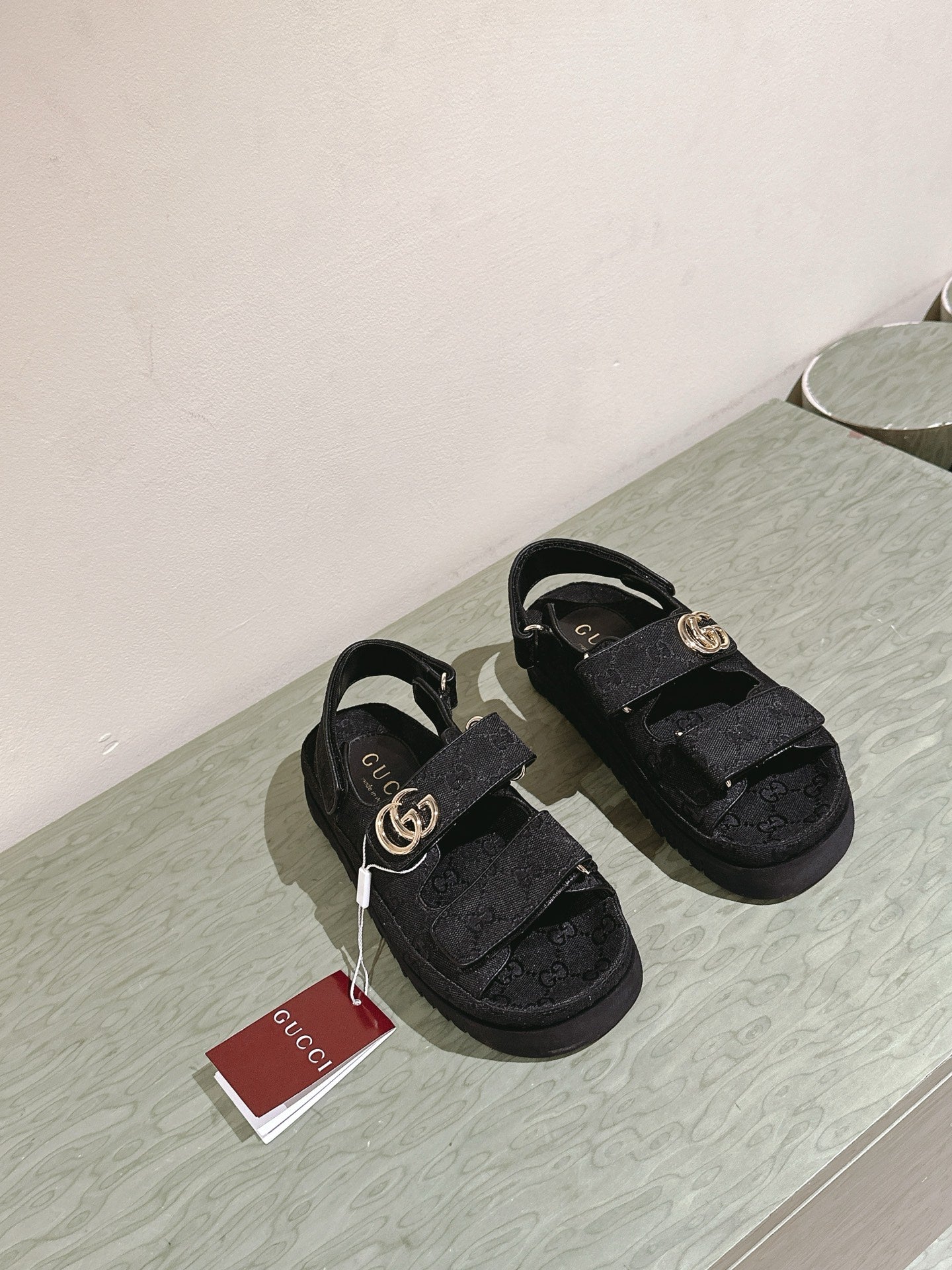 Black Gucci sandals on display with gold-tone GG buckles, front view