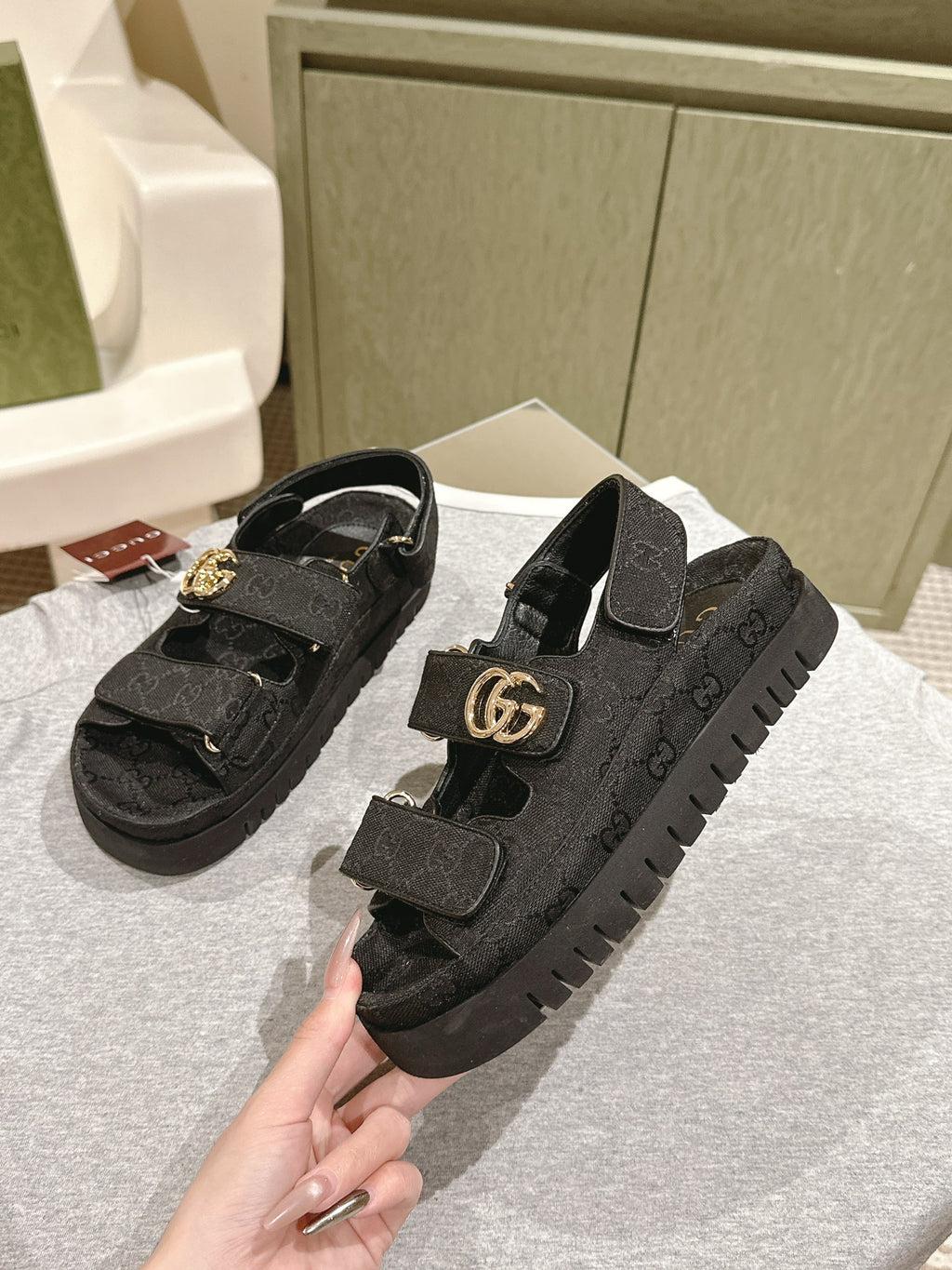 Black Gucci sandals with embossed pattern and gold-tone GG buckle, angled view