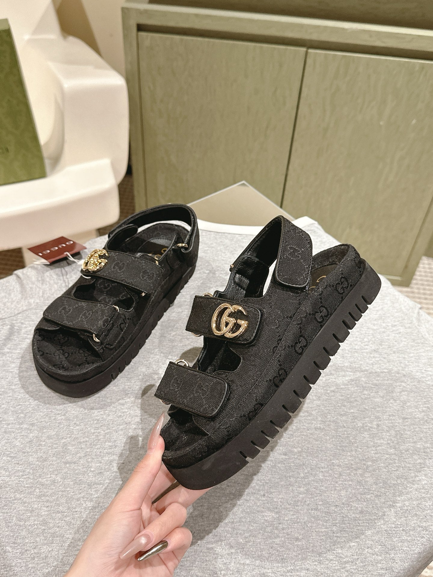 Black Gucci sandals with embossed pattern and gold-tone GG buckle, angled view