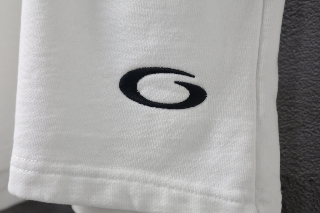 White shorts with embroidered black oval logo on the lower leg