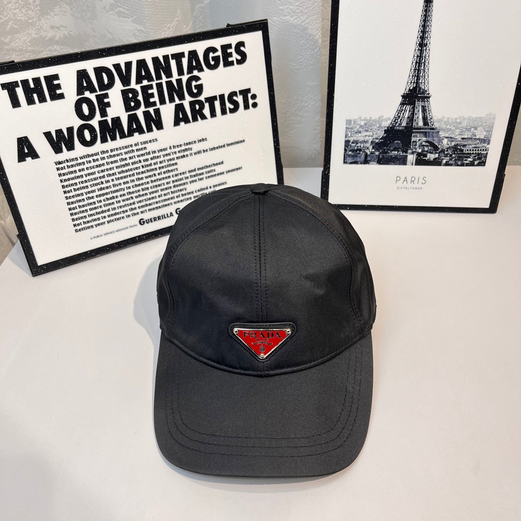 Prada cap in dark fabric with triangular logo patch and curved brim.