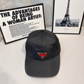 Prada cap in dark fabric with triangular logo patch and curved brim.