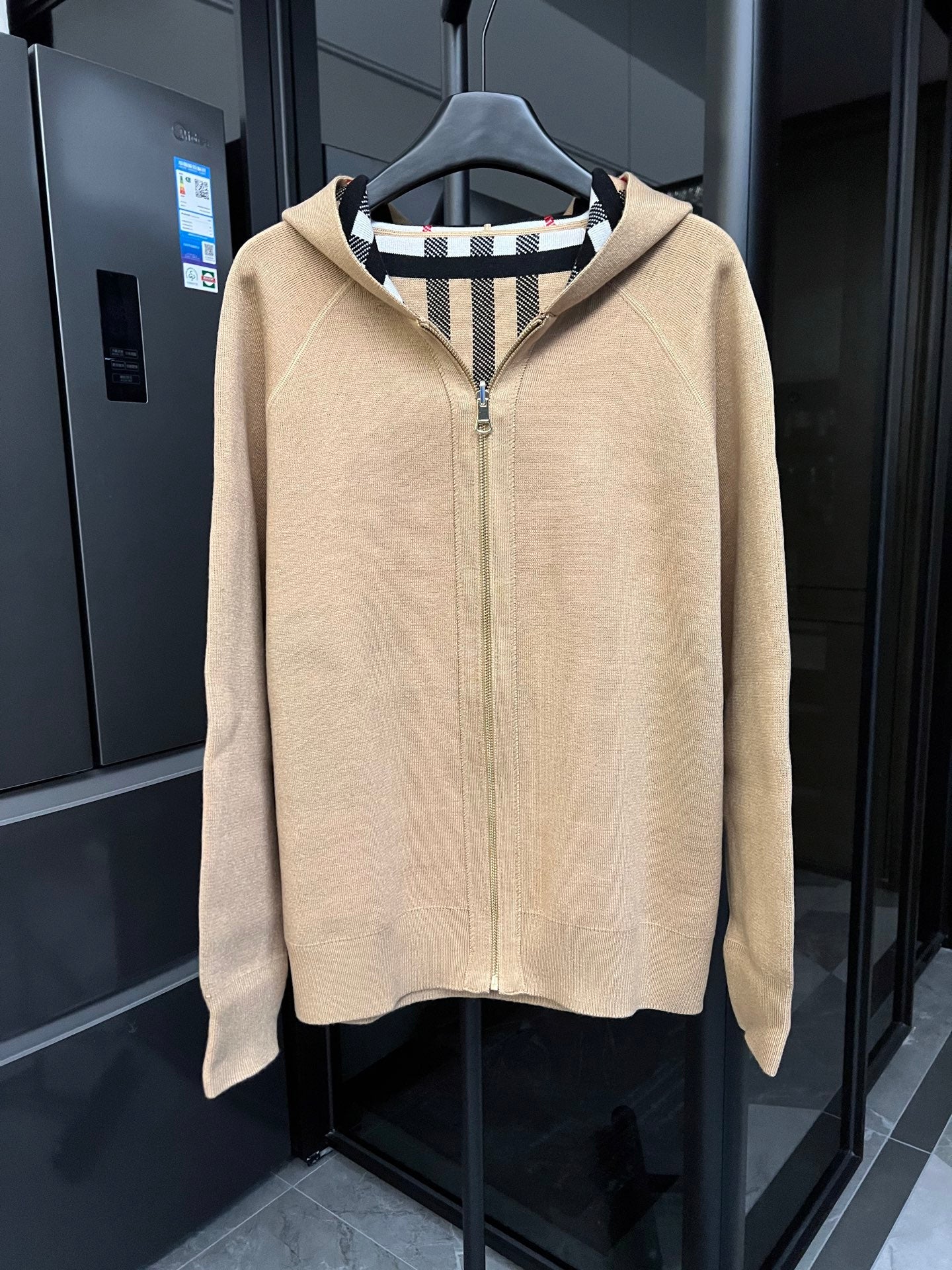 Beige zip-front sweatshirt with raised collar and black-and-white striped inner hood