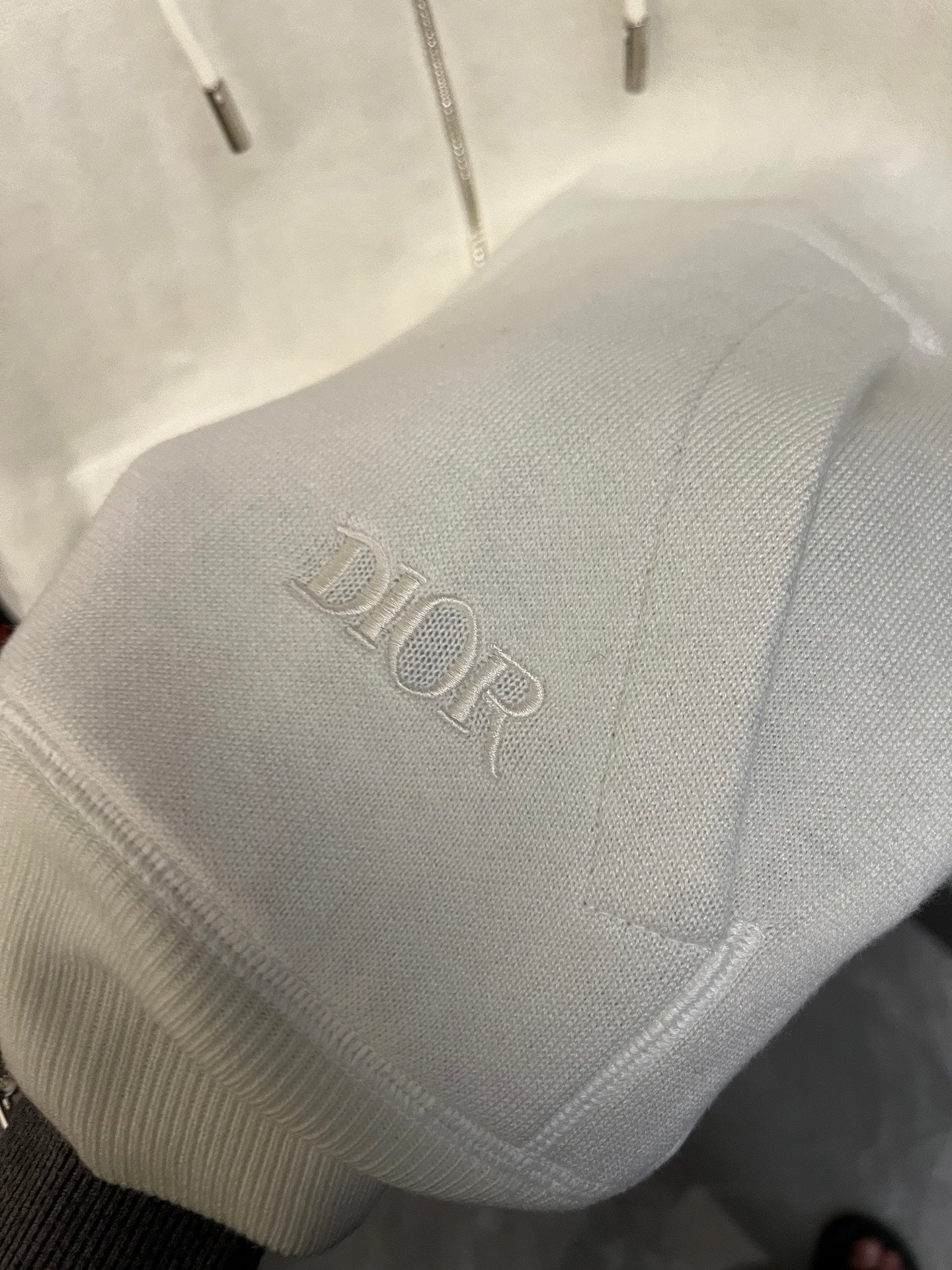 Off-white hoodie sleeve cuff with Dior logo embroidery in raised knit.