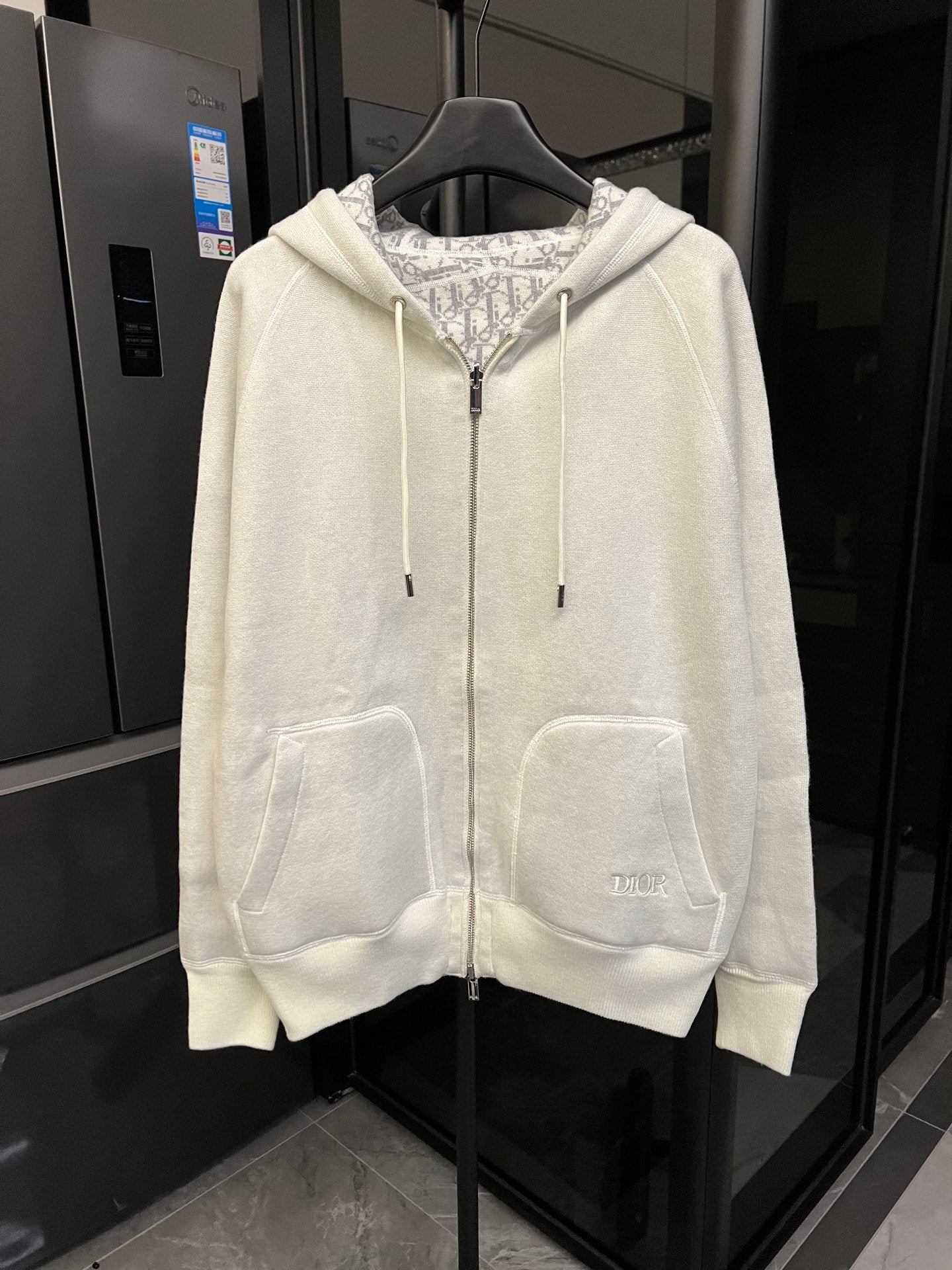 Off-white zip-up hoodie with hood, drawstring ties, and front kangaroo pockets.