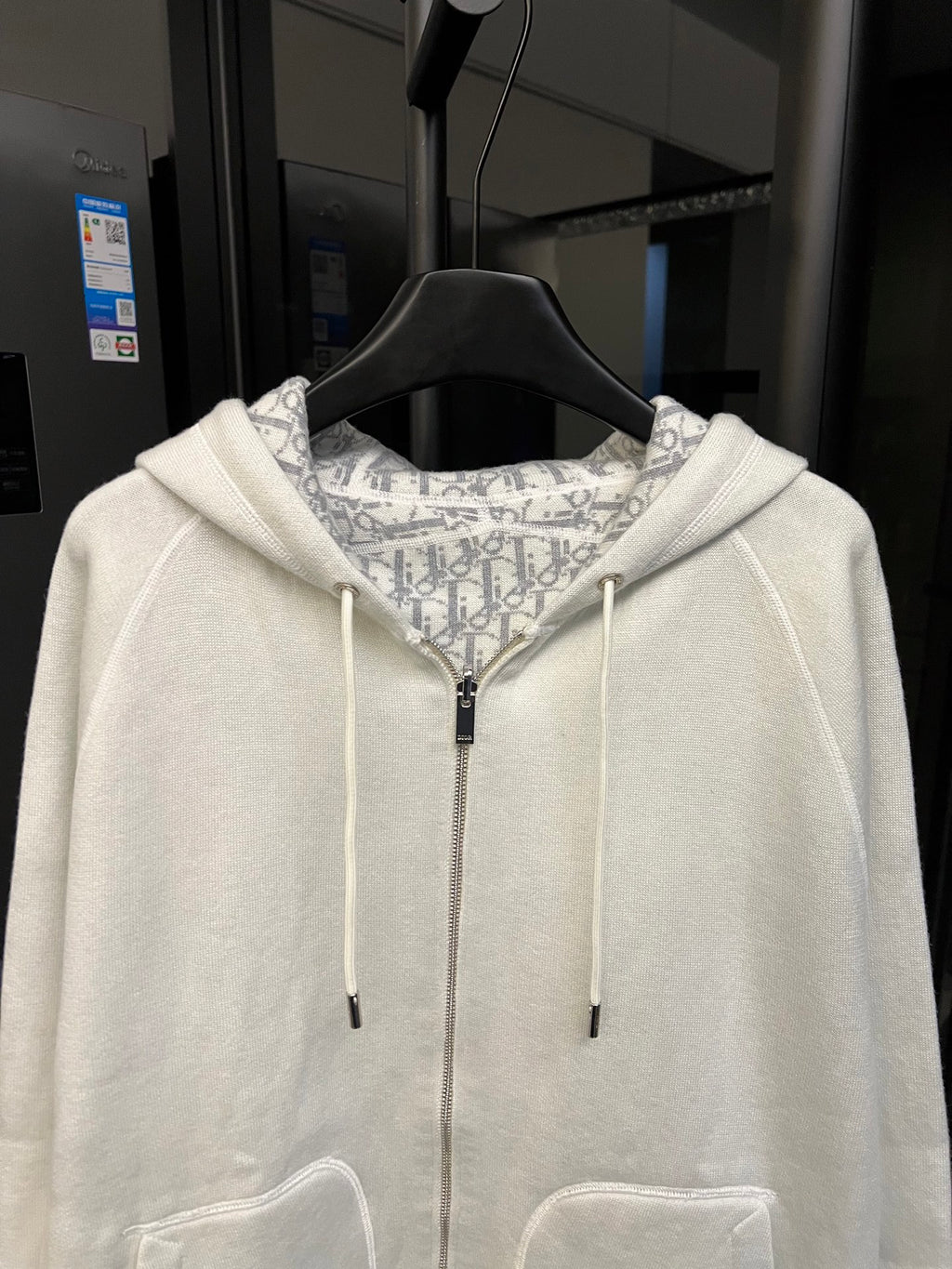 Off-white zip-up hoodie with central zipper, drawstring hood, and patterned lining.