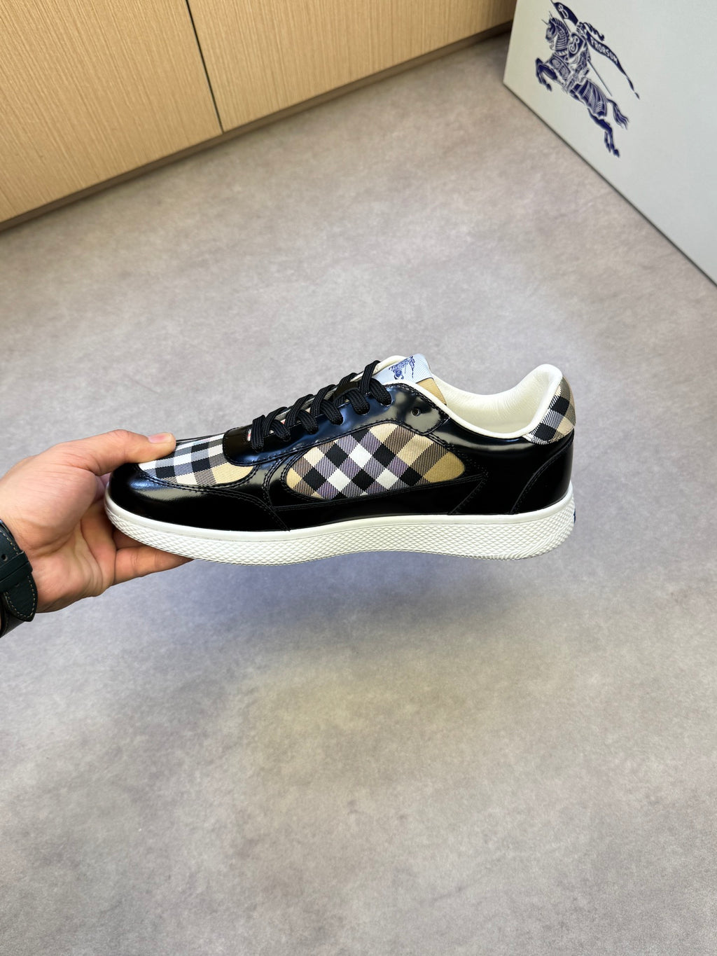 Black and white checkered low-top sneakers held by heel, white rubber sole