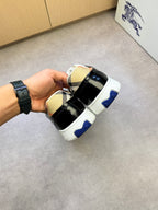 Black and white checkered sneakers held upside down, blue heel logo and white sole