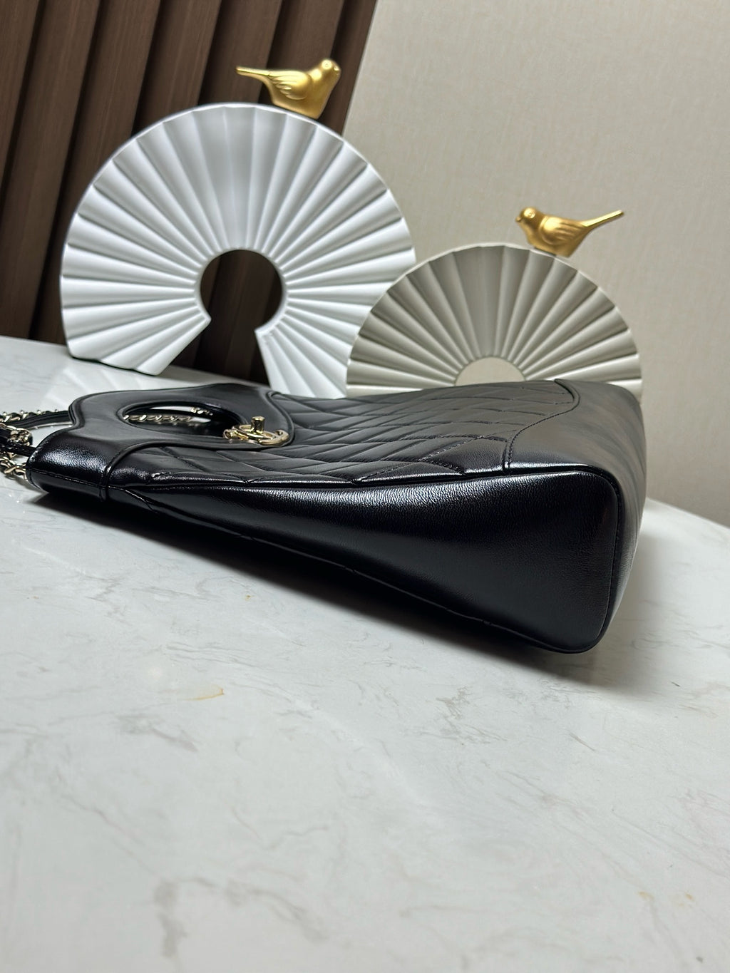 Black quilted shoulder bag with gold hardware and chain strap, angled view