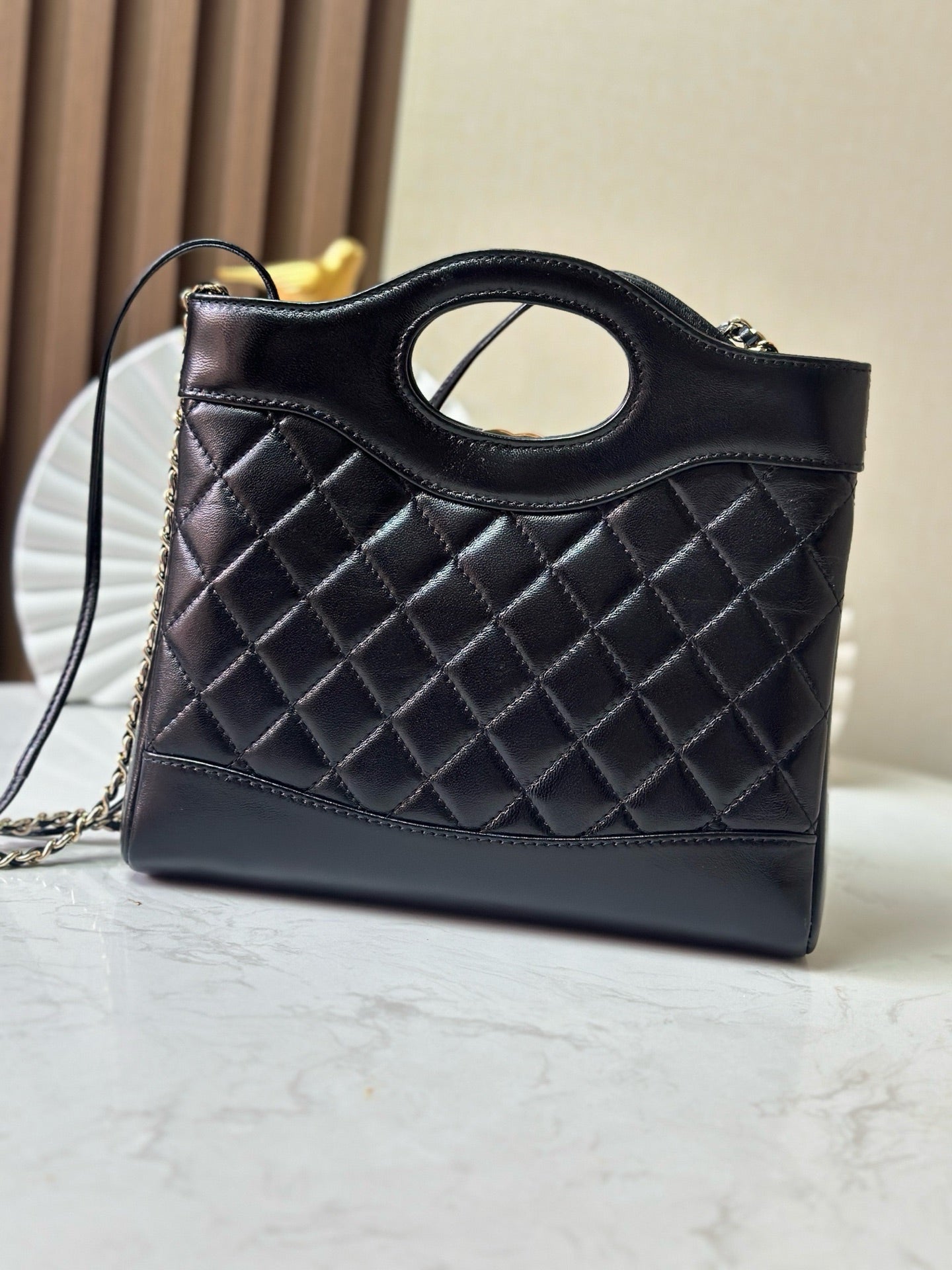 Black quilted handbag with oval logo ring top handle and gold-tone chain strap