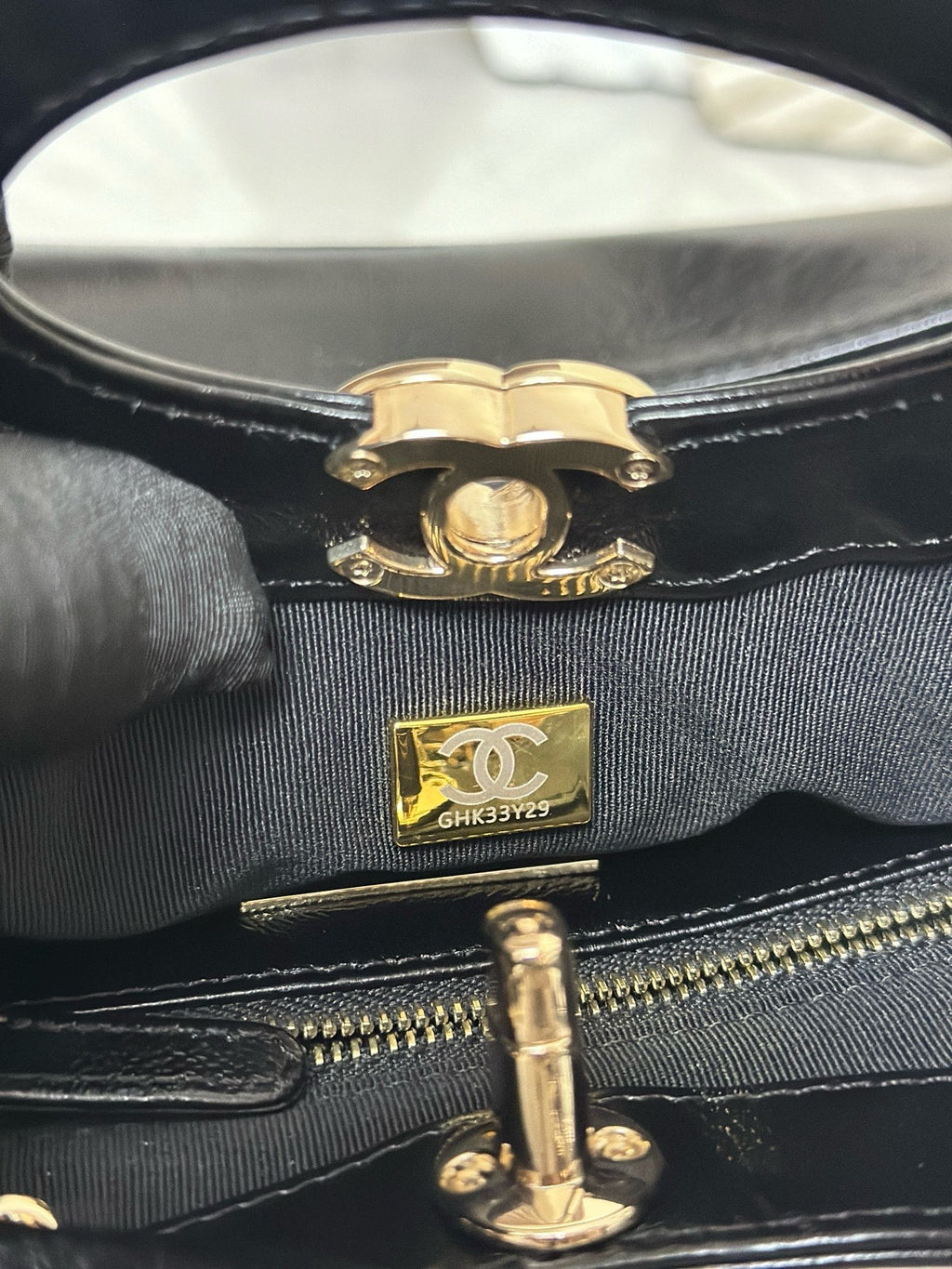 Close-up of black handbag closure with gold-tone emblem and zipper track