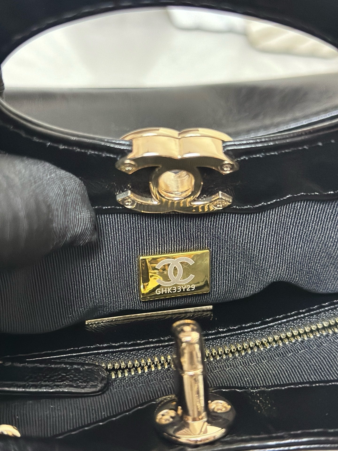 Close-up of black handbag closure with gold-tone emblem and zipper track