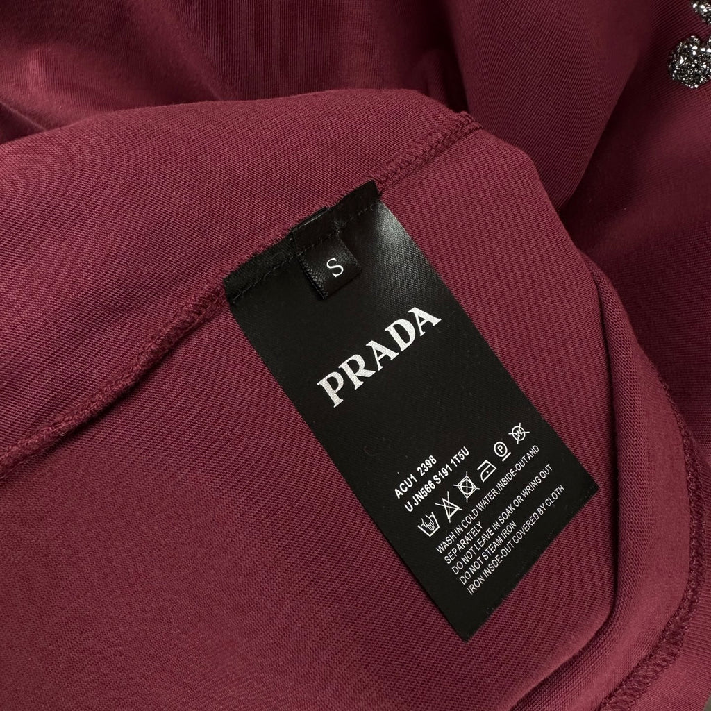 Prada T-shirt neck label and size tag on dark berry fabric.