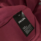 Prada T-shirt neck label and size tag on dark berry fabric.