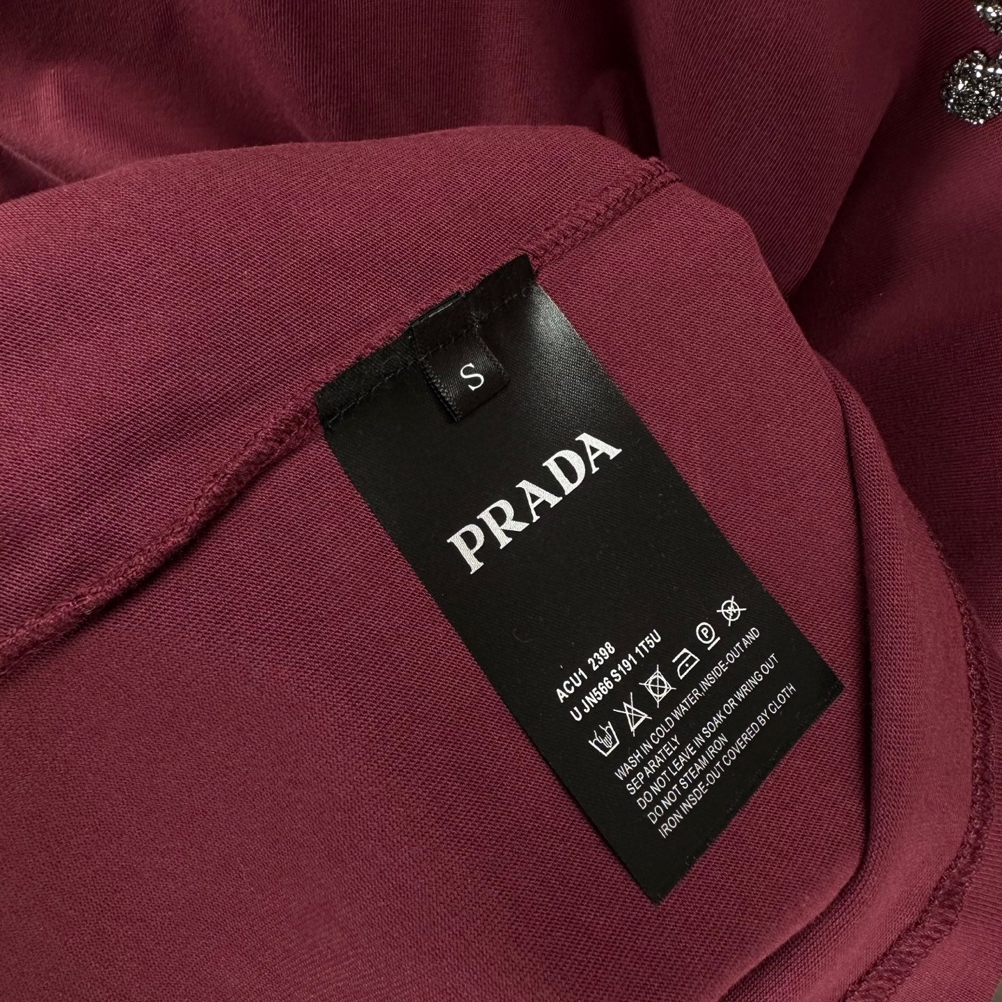 Prada T-shirt neck label and size tag on dark berry fabric.