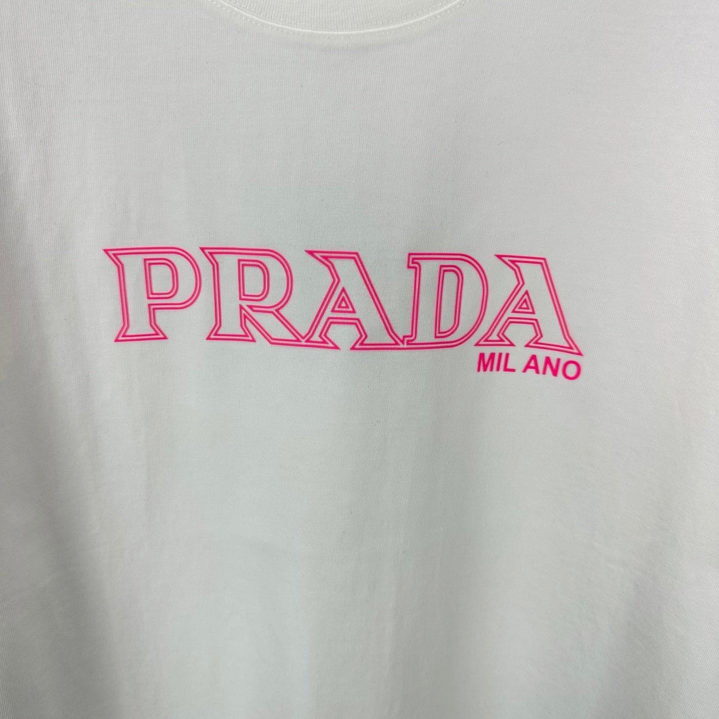 White T-shirt with large pink PRADA MIL ANO logo graphic on the front.