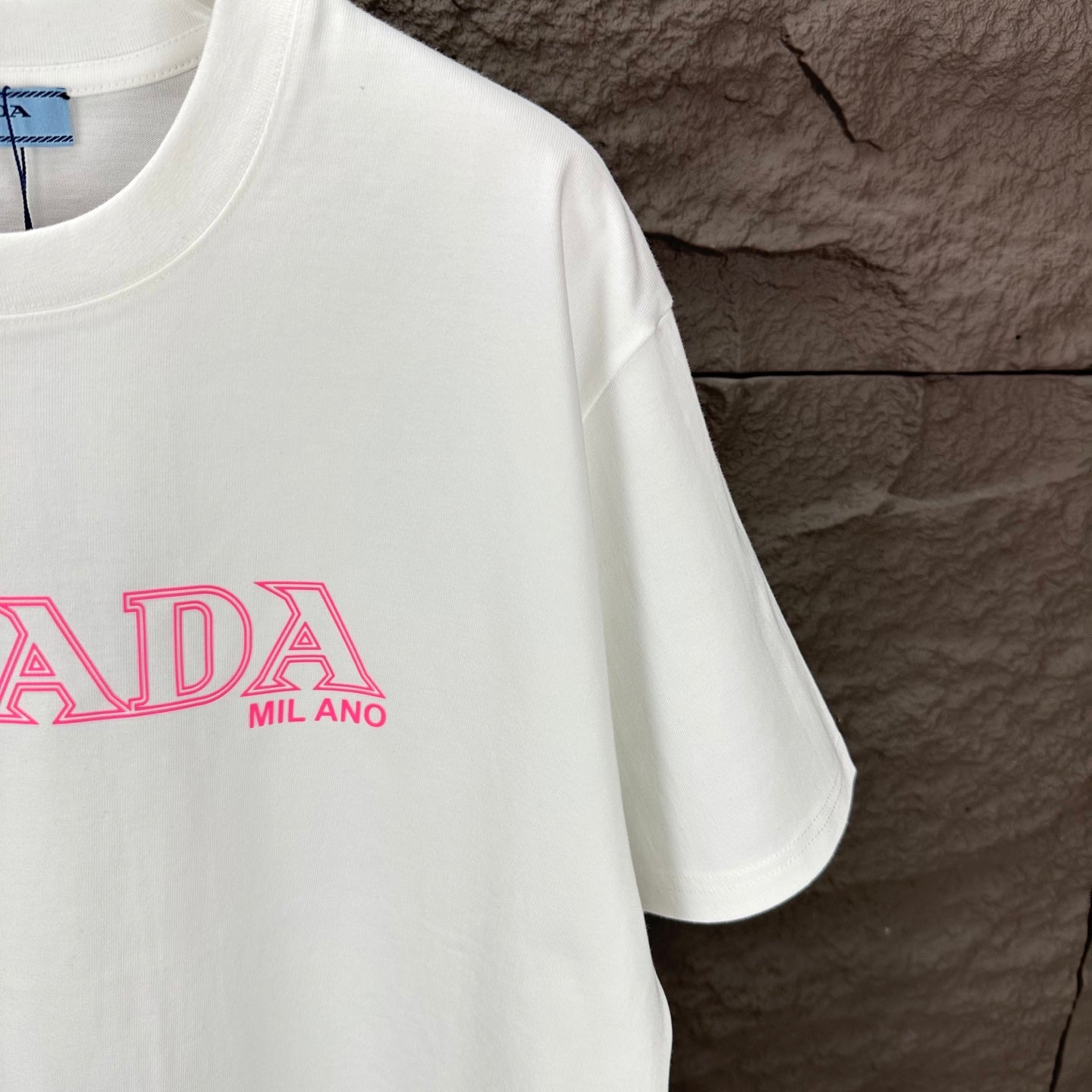 White short-sleeve T-shirt with partial pink PRADA MIL ANO logo print.