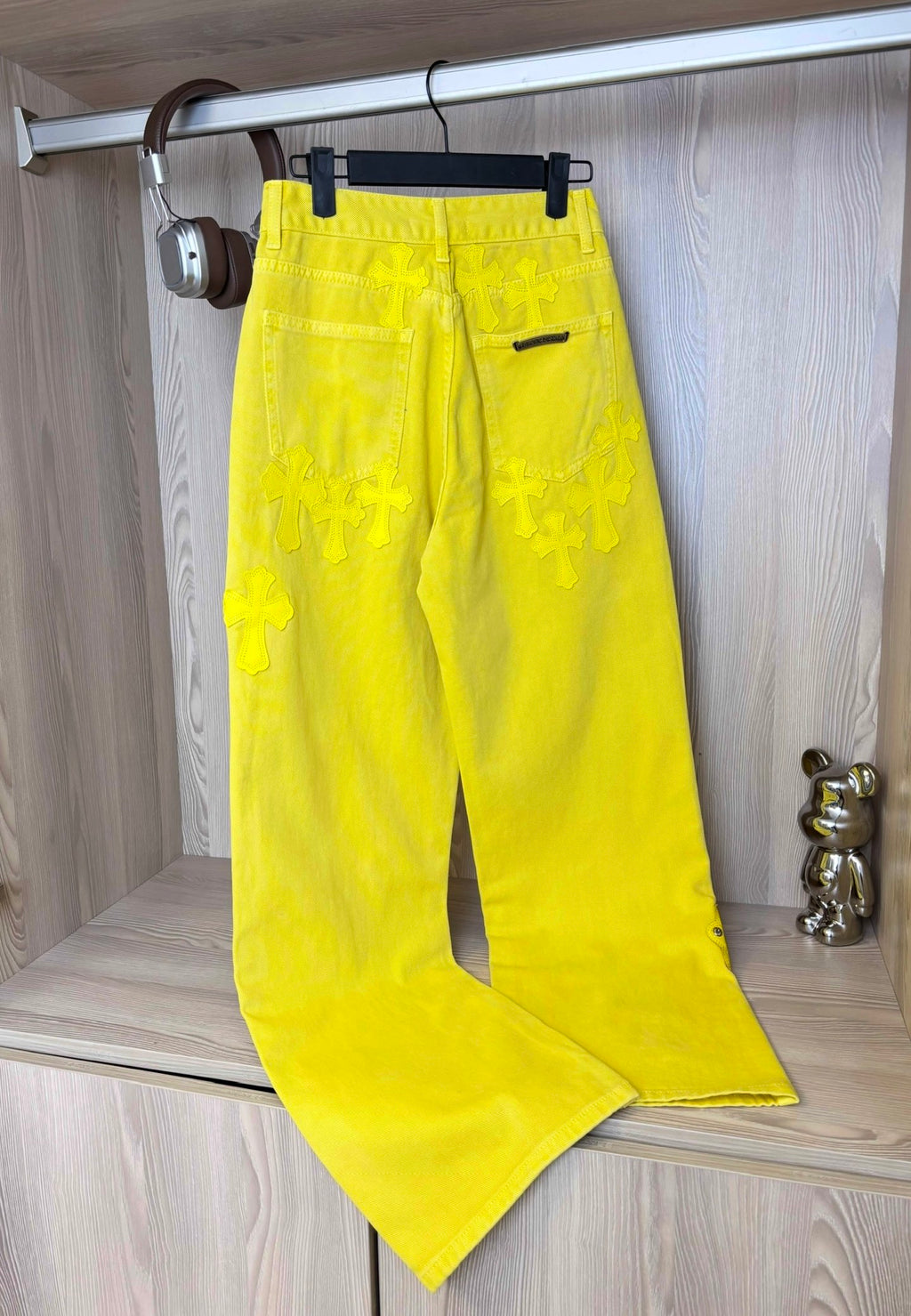 Yellow pants on a hanger with belt loops, button fly, and decorative cross patches.