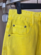 Yellow pants close-up of waistband, front pockets, and metal button accents.