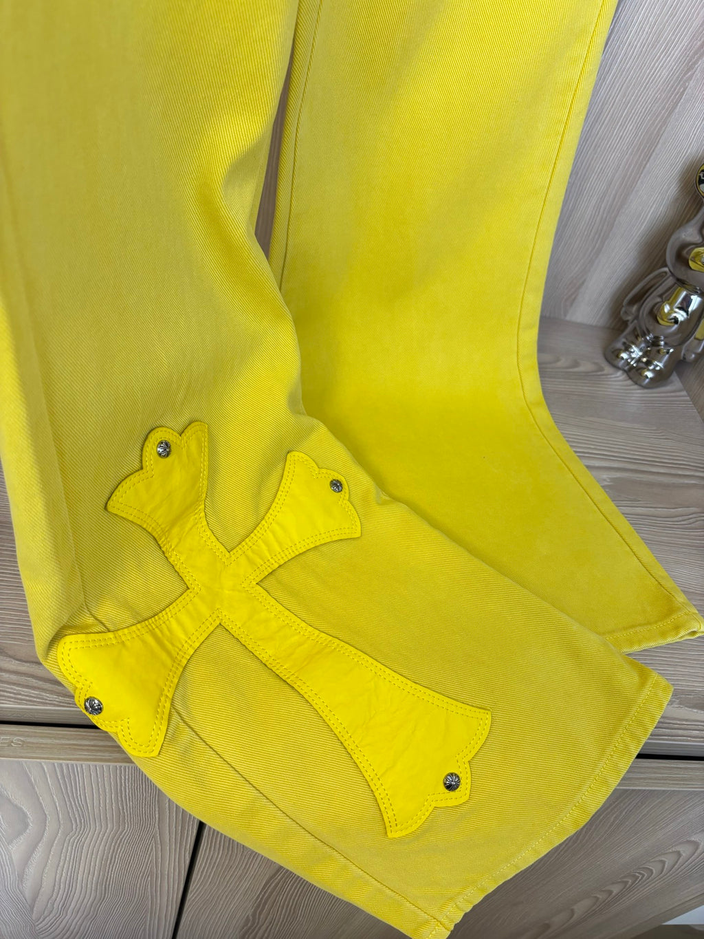 Yellow pants close-up with cross appliqué near knee and five-pocket style details.