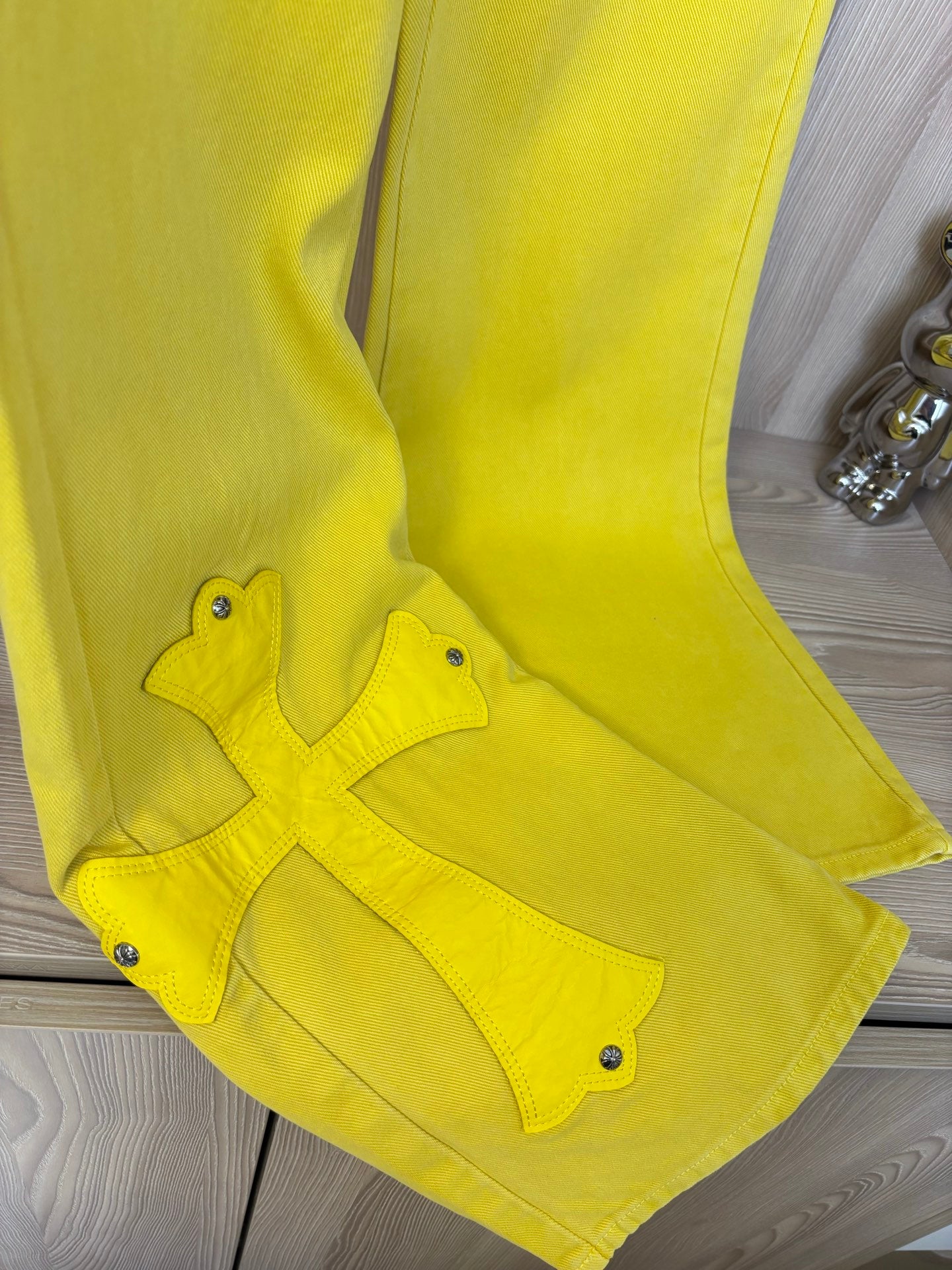 Yellow pants close-up with cross appliqué near knee and five-pocket style details.