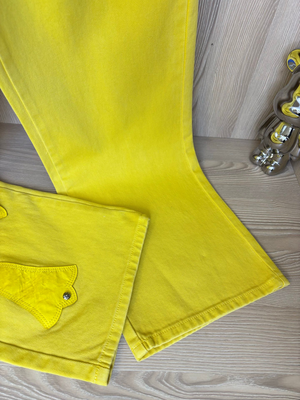 Yellow pants hem and back pocket with button, featuring cross patch stitching.